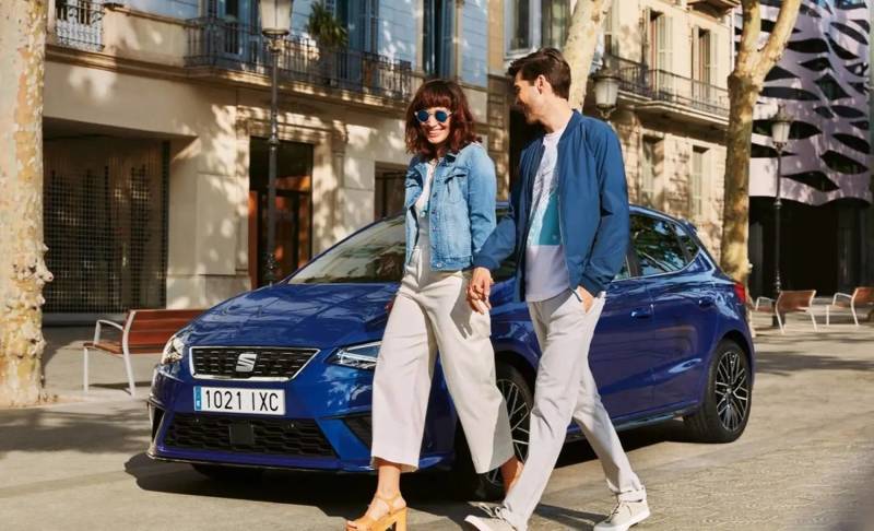 Smiling couple walking hand in hand past a parked blue car