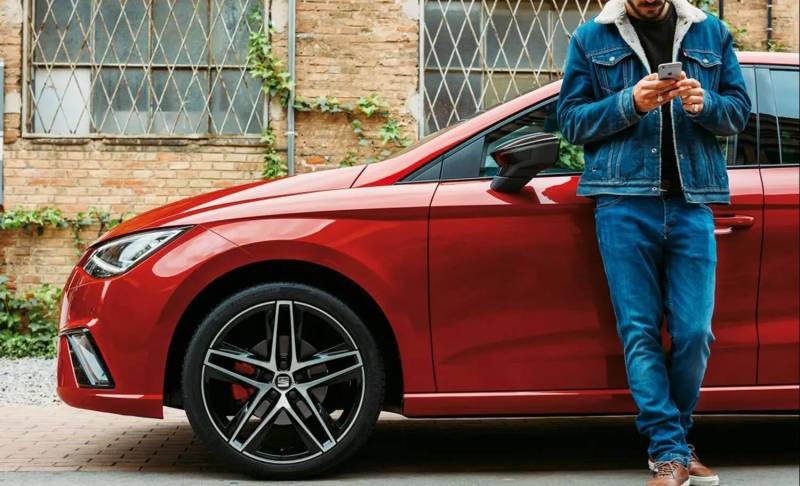 Man leaning against a red car while using his phone
